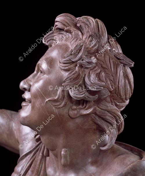 Statue of drunken Faun in antique red. Detail of the face