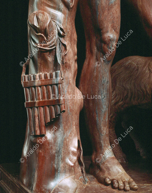 Statue of drunken Faun in antique red. Detail of the flute